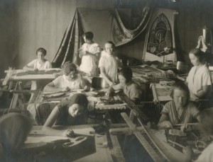 Бригада мастериц-вышивальщиц выполняет заказ от ЦК Союза горнорабочих СССР к Х годовщине Октябрьской революции. Александра Кольцова-Бычкова стоит в центре, ее младшая сестра Зинаида стоит справа. Фотография для журнала